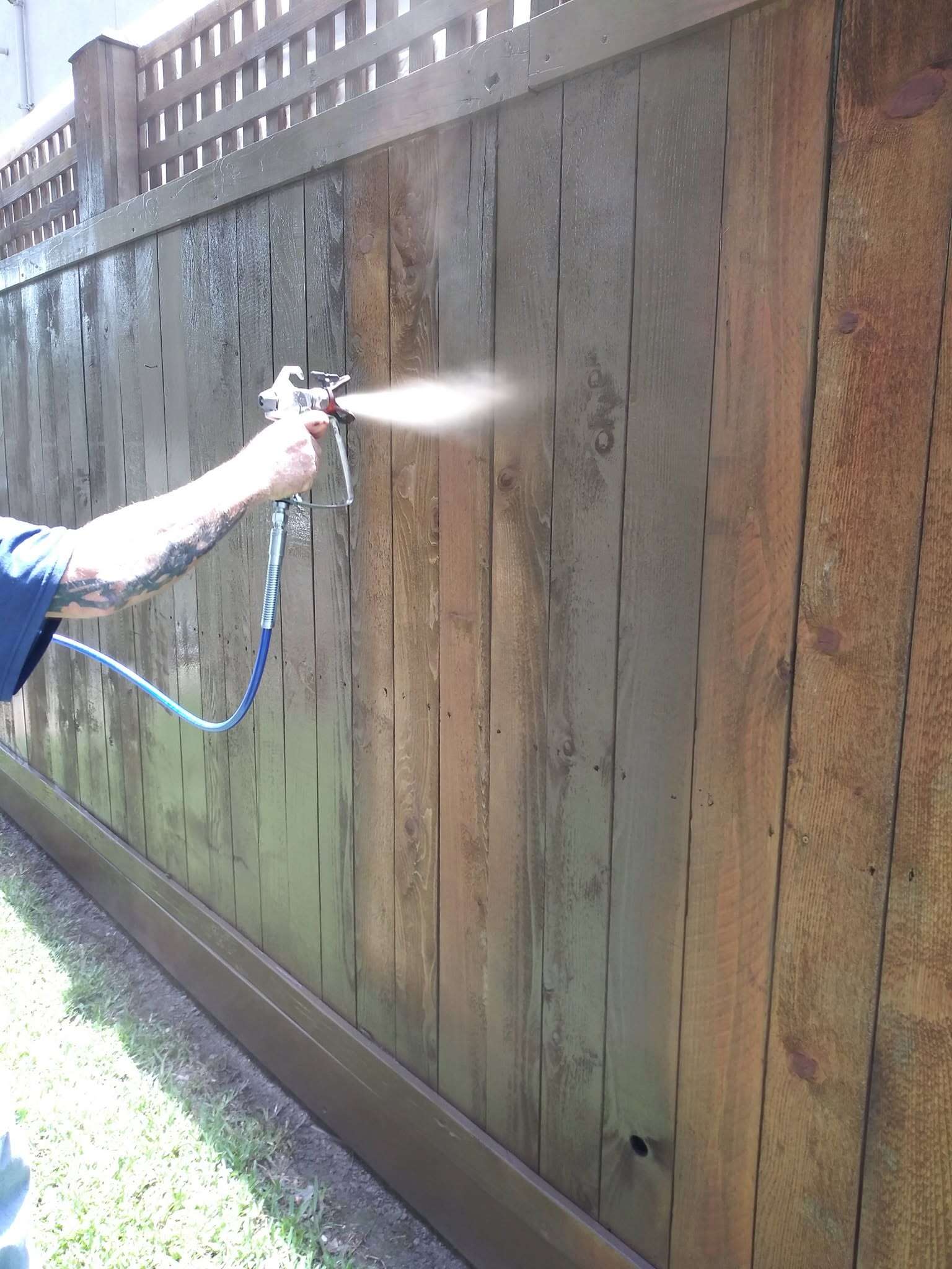 Professional spraying stain evenly across a wood privacy fence